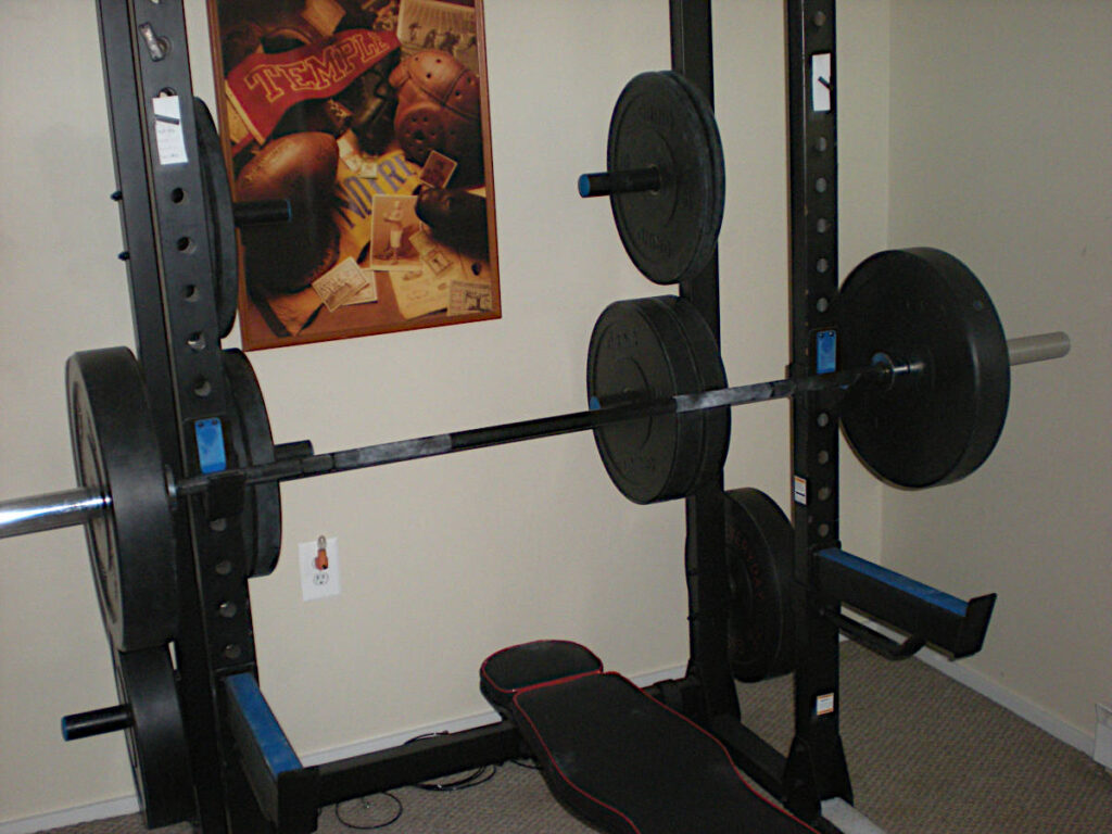 Grind Chaos 4000 Half Rack, bumper plates, Olympic bar, and bench. Temple/Notre Dame picture on the wall.