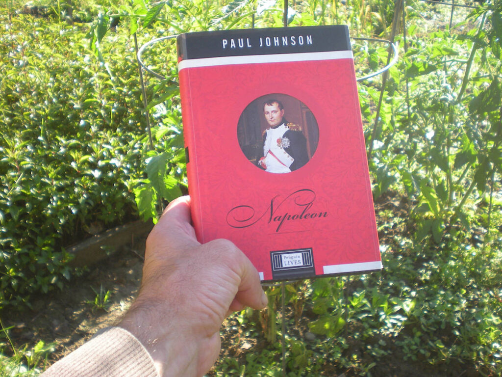 Book (haven't read it yet): "Napoleon" by Paul Johnson* Background image: Garden 2026 — peppermint to the left, tomatoes directly behind book, basking in the sun on Summer Solstice Morning 2026.